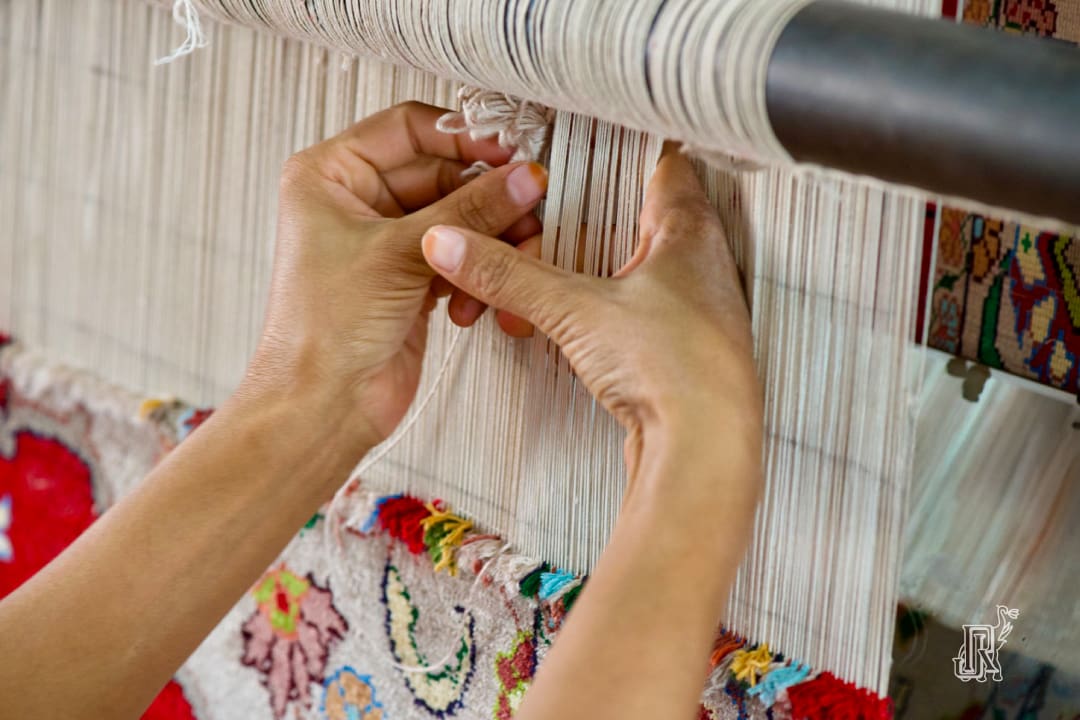 Close-up of an artisan's hands meticulously weaving an intricate Indian rugs JR Exports on a traditional loom, showcasing fine craftsmanship and vibrant patterns.